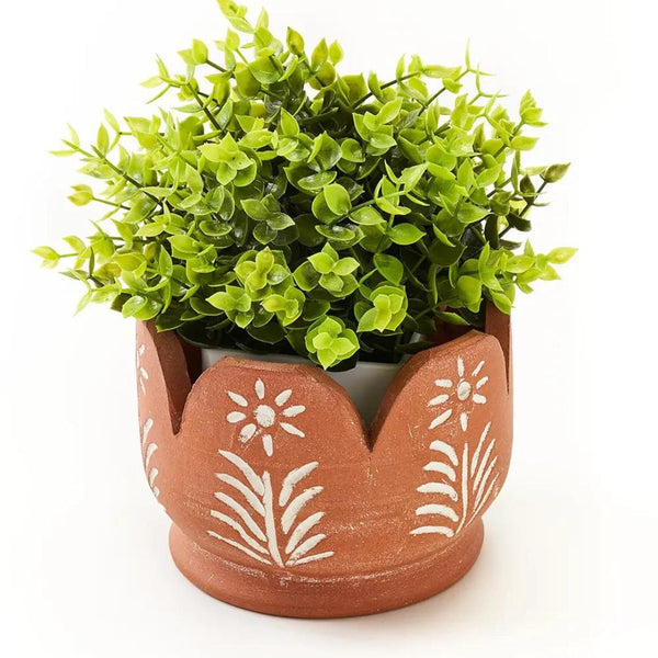 A brown planter with a white design on it and a green plant inside
